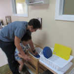 A teacher teaching a child how to wash plates (150x150)