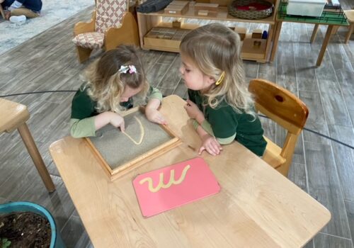 Two girls learning how to write in cursive using sand